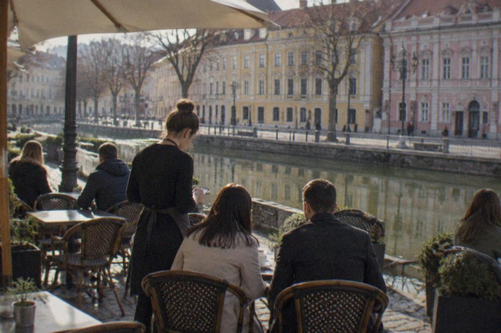 A cafe terrace in a historic square where a server takes an order from a table of visitors
