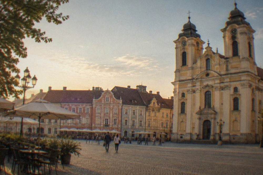 A baroque cathedral facade and pastel townhouses seen from a cobblestone square with cafe tables