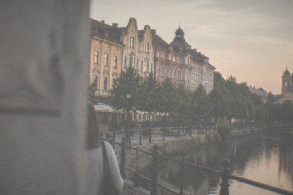 A riverside promenade along a canal with a domed cathedral in the background at dusk