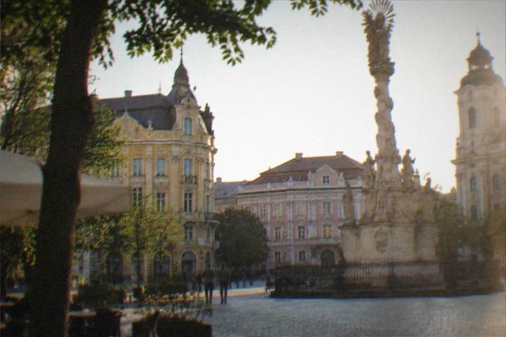 A historic square with baroque facades and a plague column seen from ground level