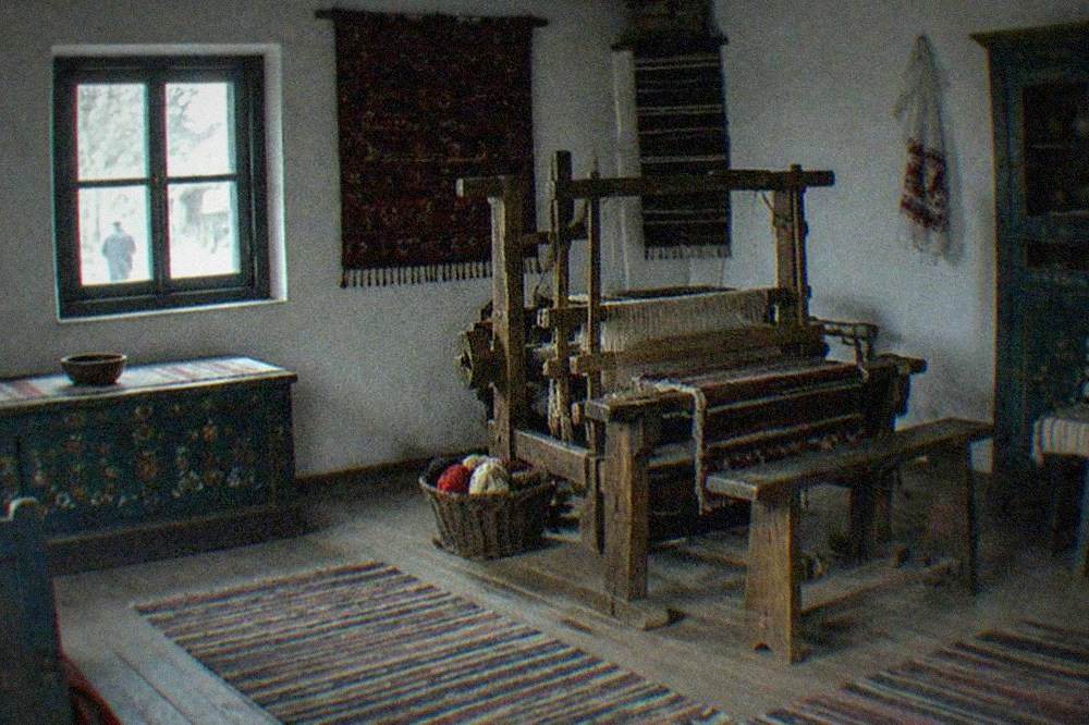 A furnished village house interior with a loom, painted wooden furniture and woven textiles on display