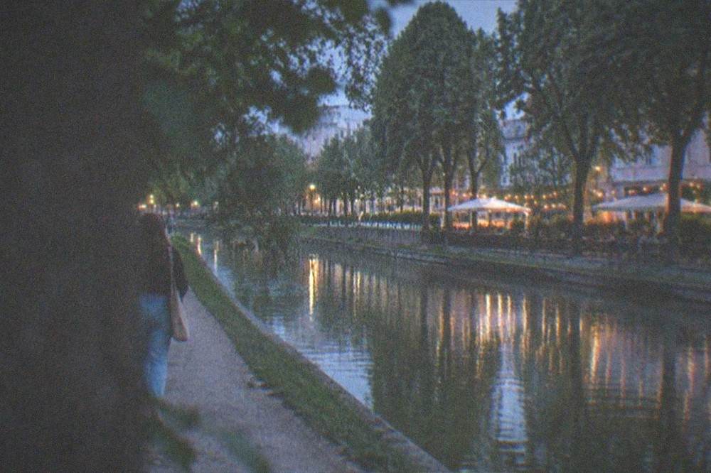 A canal-side terrace with tables and string lights at dusk, reflected in the water