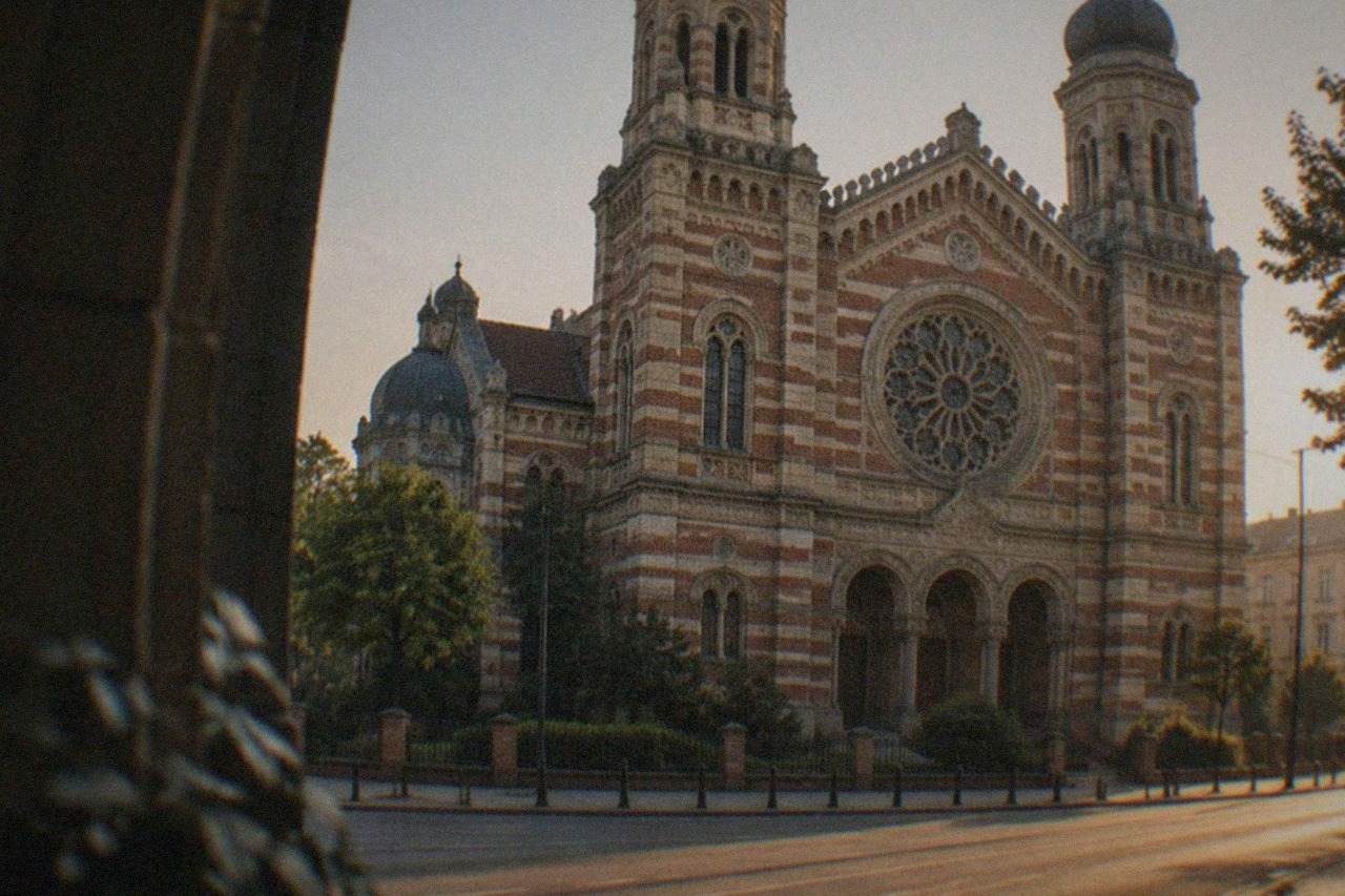 Ornate synagogue facade with striped arches and a domed tower beside a quiet street