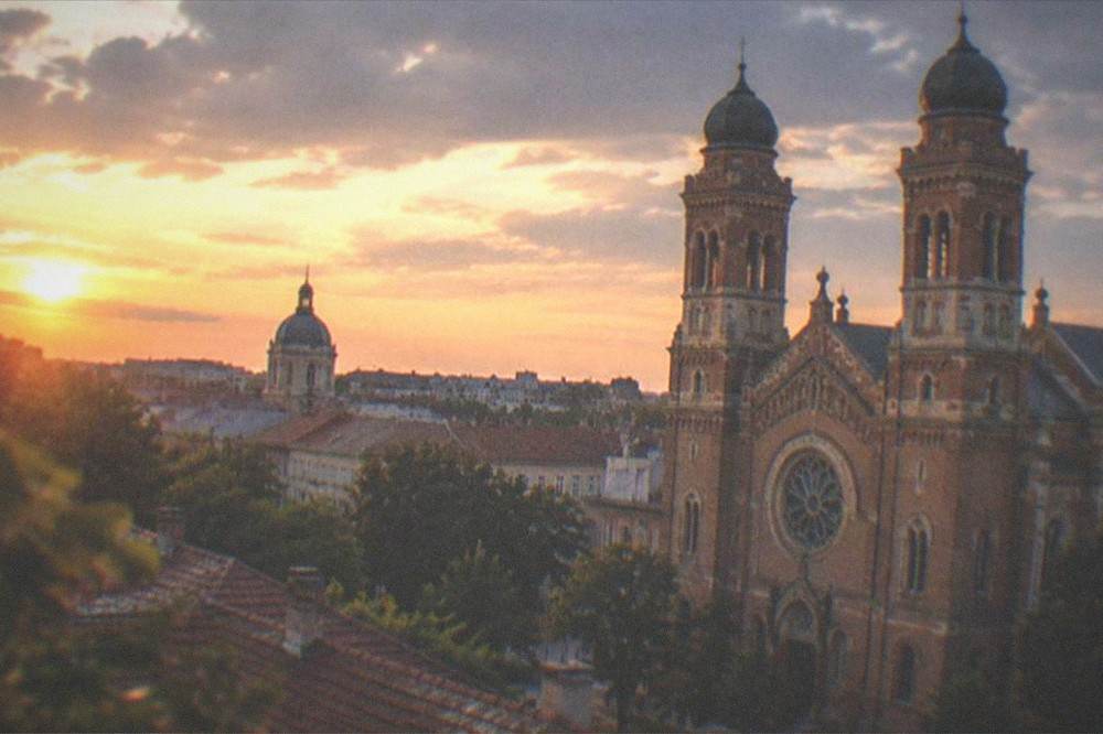 Golden hour view over rooftops toward a domed tower in the Fabric district