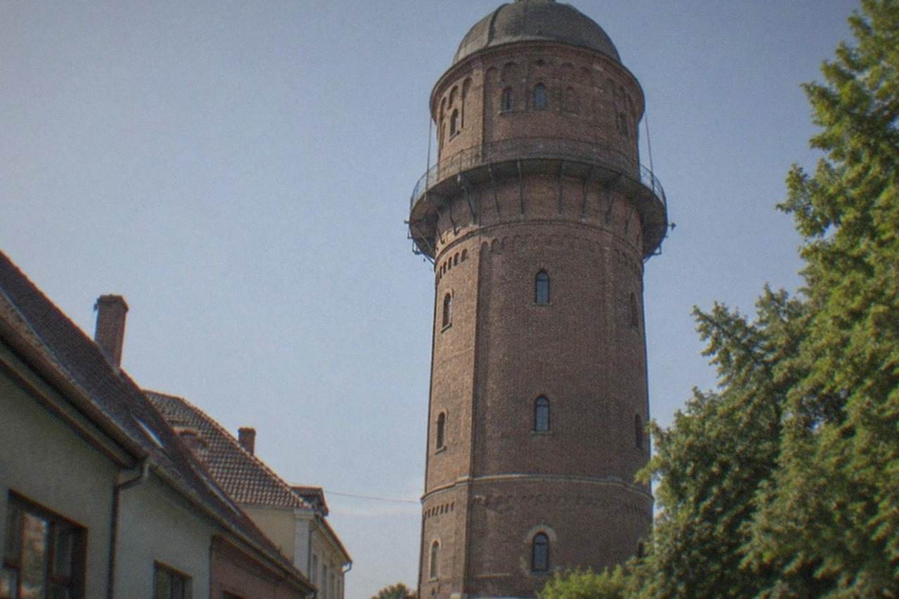 A brick water tower rising over the low rooftops of a historic neighborhood in Timisoara