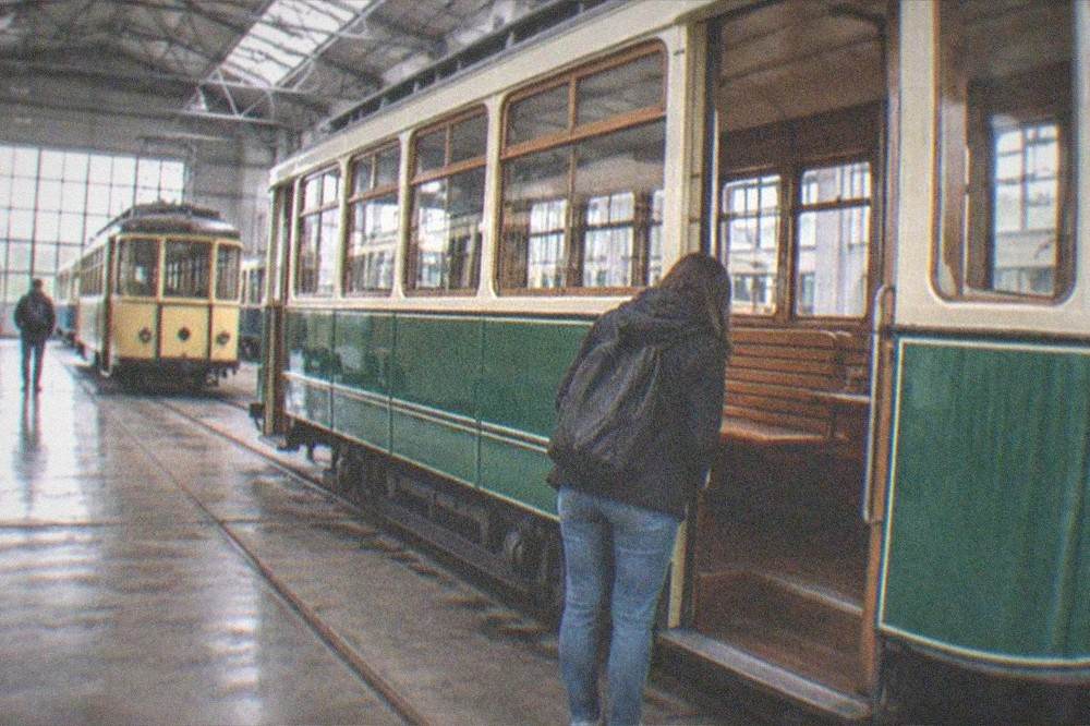 A visitor studying the interior of a restored vintage tram with wooden seats