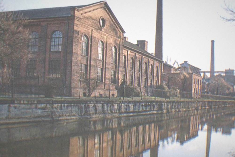 Old brick industrial building with arched windows reflected in canal water