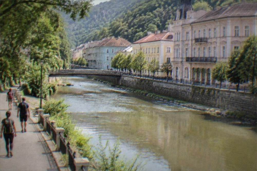 Travelers walking with day packs along a riverside path in a mountain town