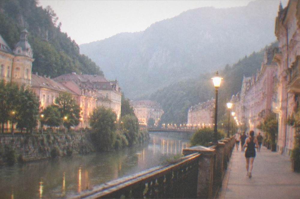 A historic spa town main street at dusk with lit facades and mountains in the background