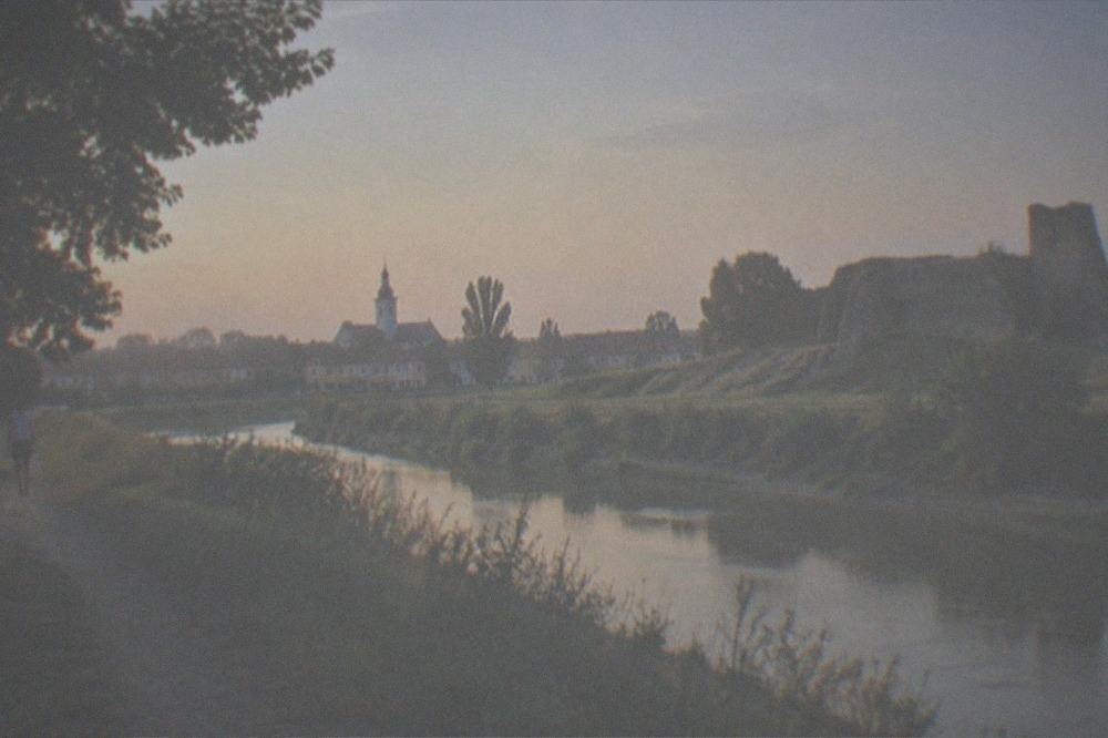 Golden late-summer light over harvested fields and a distant village church tower