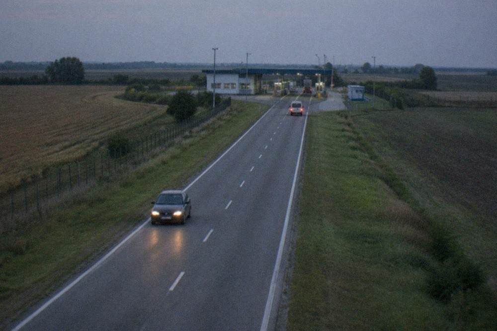 Road stretching across flat farmland toward a small border checkpoint building