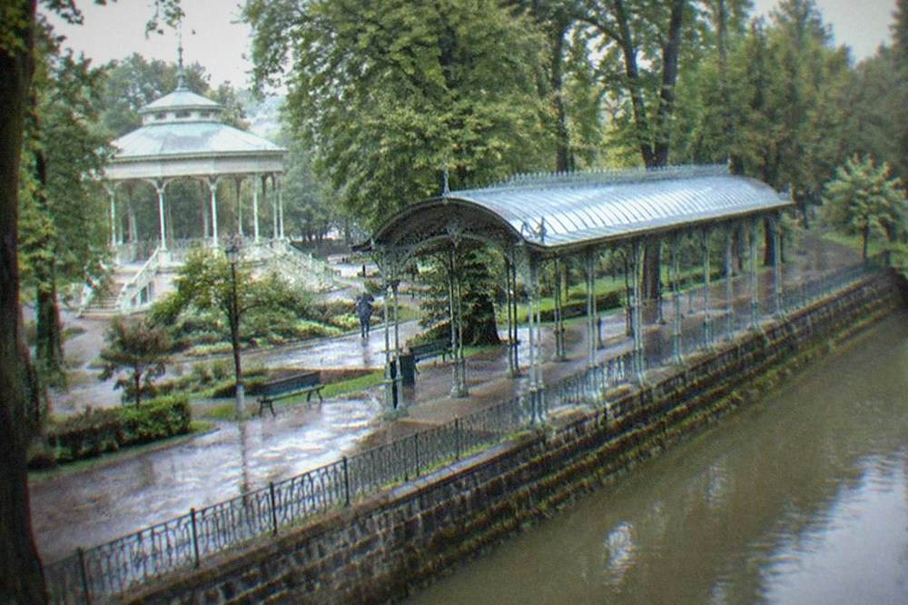 An ornate covered colonnade with decorative ironwork standing among park trees