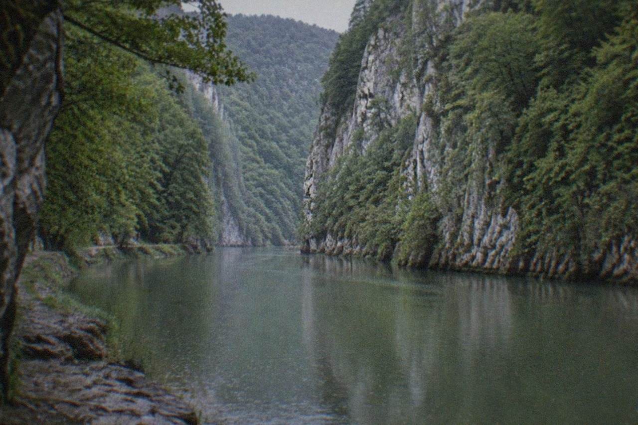 A river winding between steep forested limestone cliffs in a gorge in western Romania