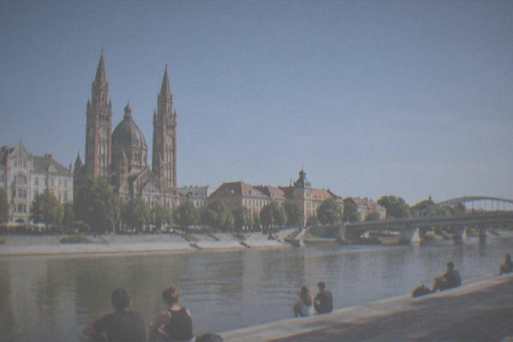 People relaxing on a riverside promenade with the Tisza river and city bridges in view
