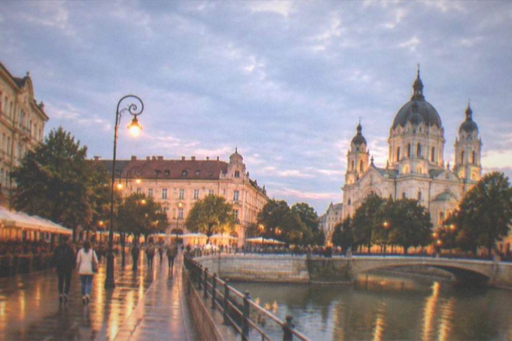A lit-up city square at dusk with pedestrians and cafe terraces under historic facades