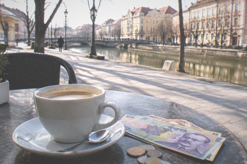 Romanian banknotes and coins lying on a cafe table beside a coffee cup