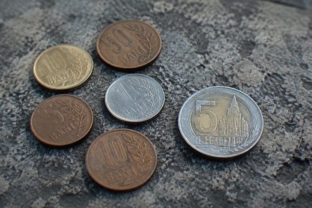 A handful of Romanian bani coins and a five lei coin on a stone surface