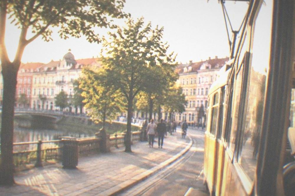 A tram moving down a street in Timisoara with a passenger reading a sign at the stop