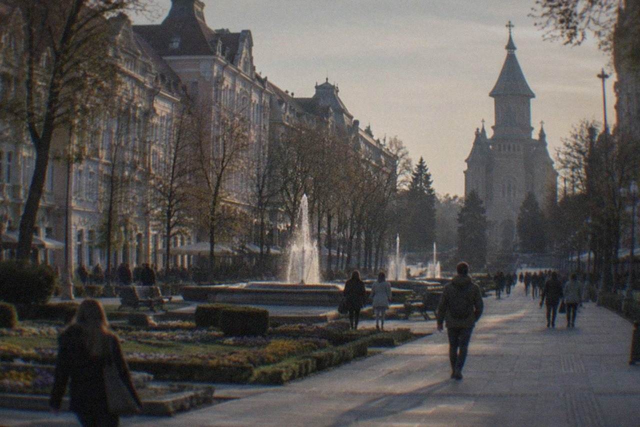 Pastel-colored baroque buildings around a European square at golden hour with people walking