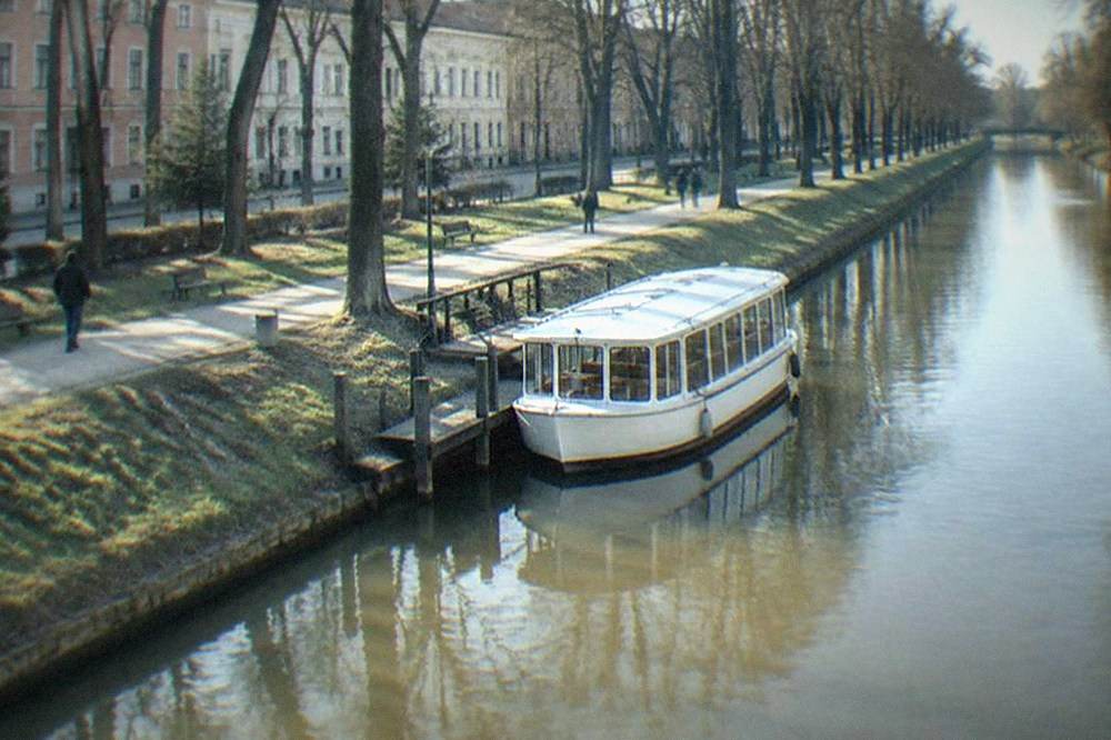 A small white vaporetto boat moored at a wooden pier on the Bega canal