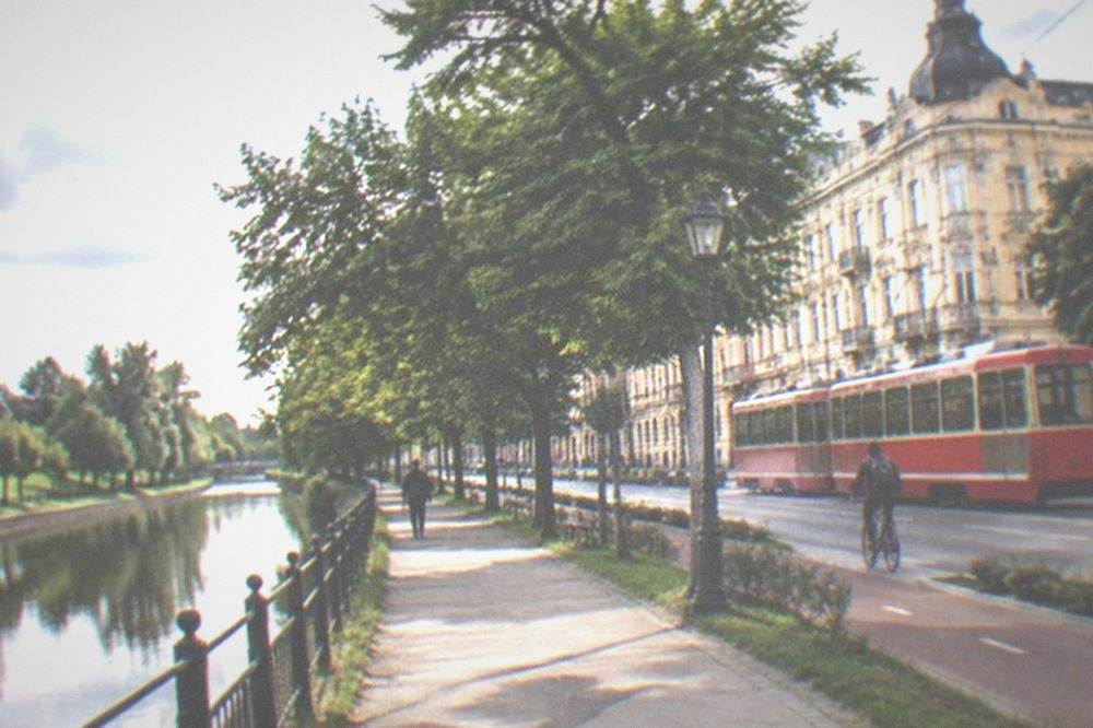 A red tram passing a bicycle lane on a city street with secession-style buildings