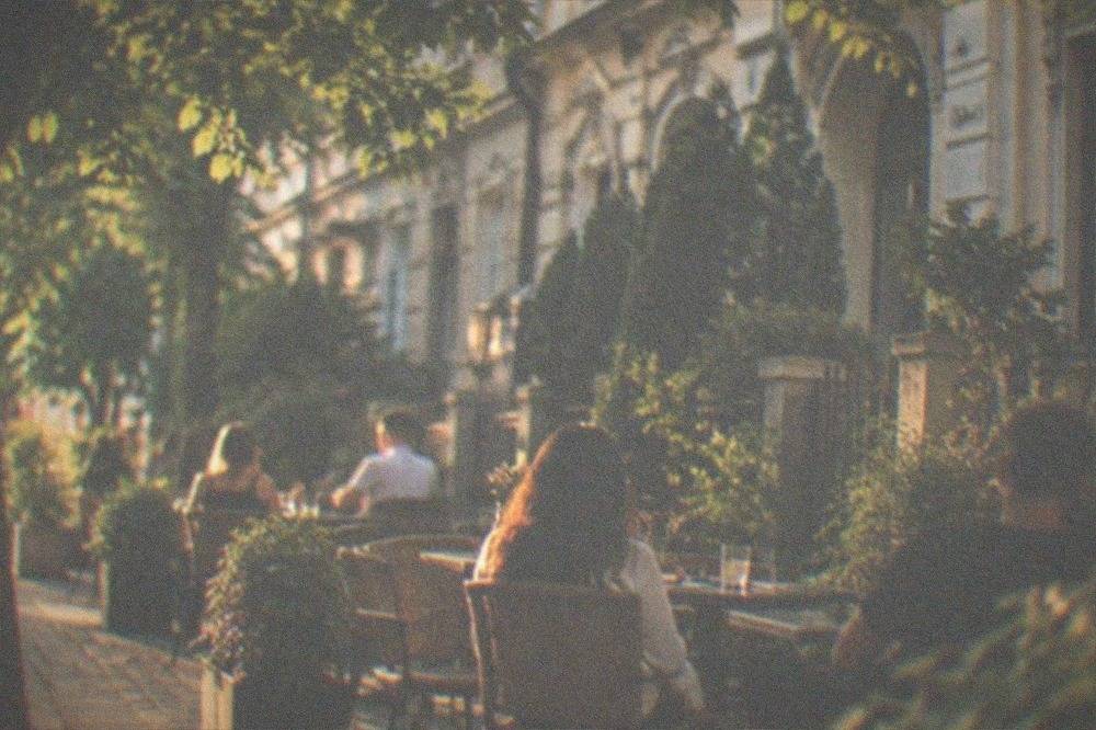 People sitting at outdoor cafe tables under trees on a street in the Elisabetin neighborhood of Timisoara