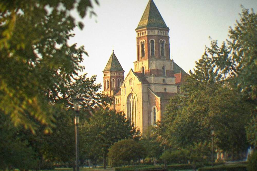 The brick facade and towers of the Millennium Church in Timisoara seen from a tree-lined square