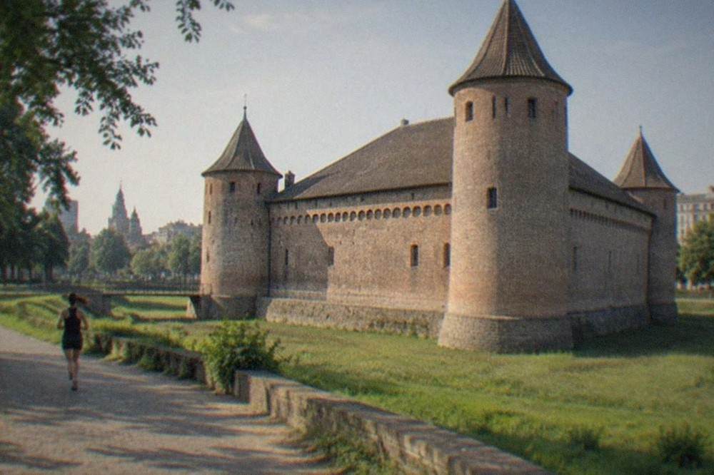 An old stone castle keep with towers, surrounded by parkland and city buildings