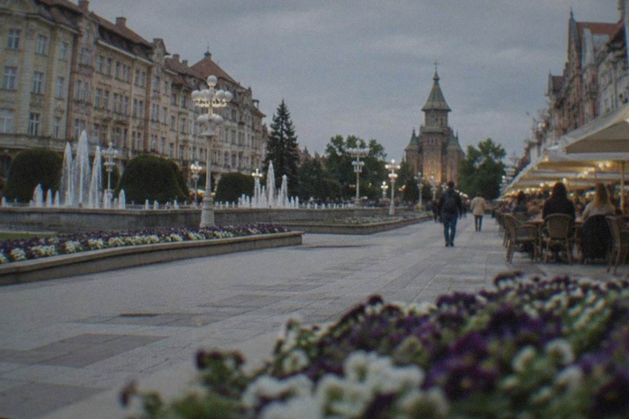 People sitting at outdoor cafe tables on a lit city square in the evening