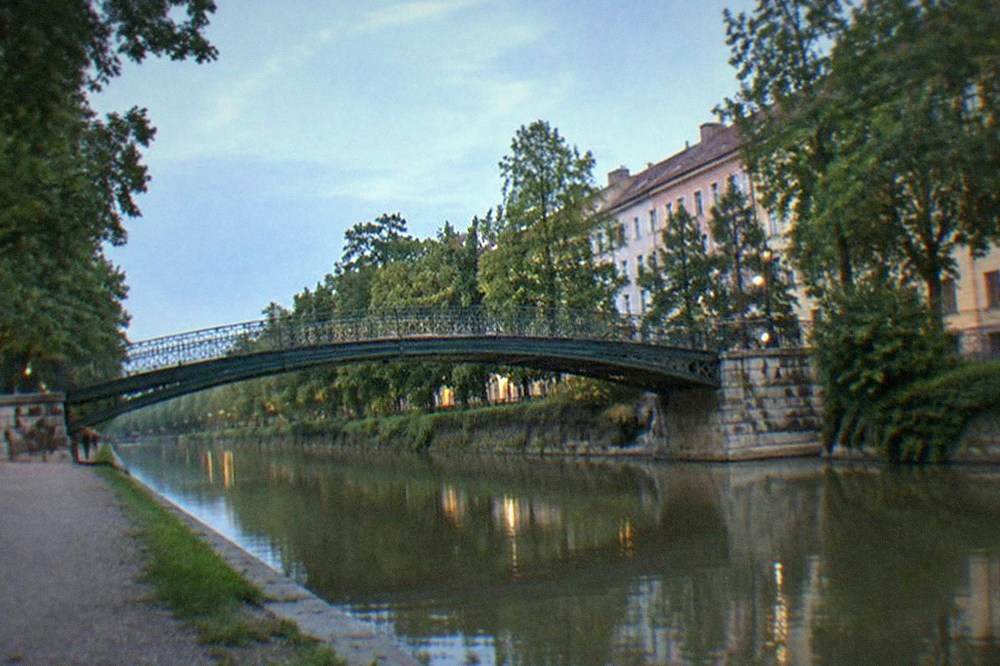 Footbridge crossing the Bega canal between parkland and city buildings in Timisoara