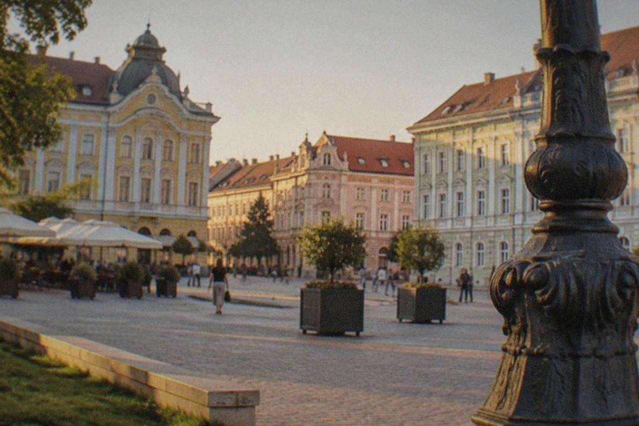 Pastel-colored baroque buildings framing a wide old town square in Timisoara at golden hour