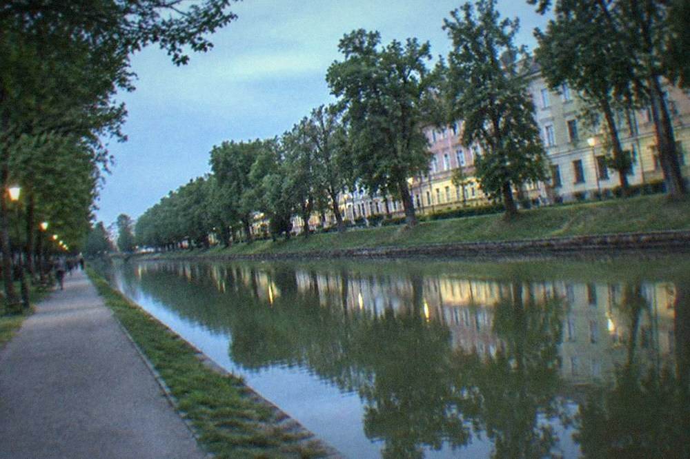 Tree-lined walking path along the Bega canal in Timisoara with benches and calm water