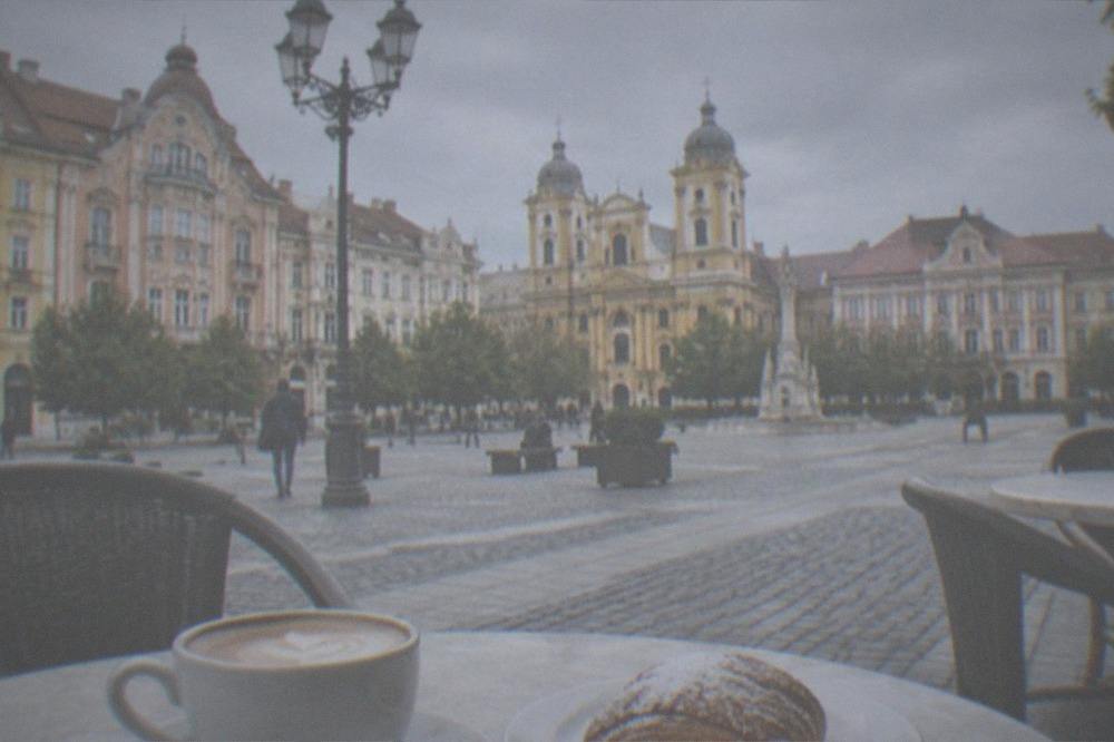 A cup of coffee and a pastry on a cafe table in a Timisoara old town square