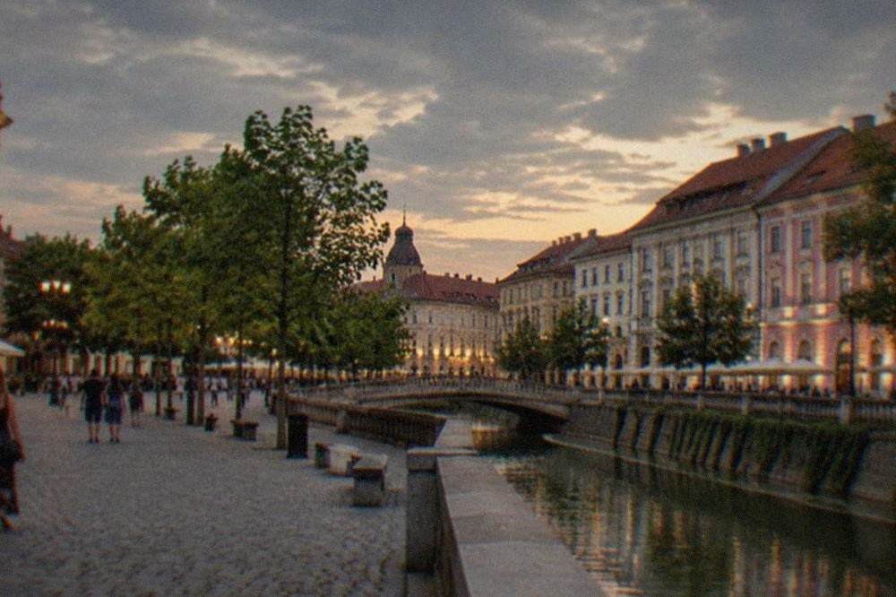 A wide city square at dusk with illuminated facades and people strolling