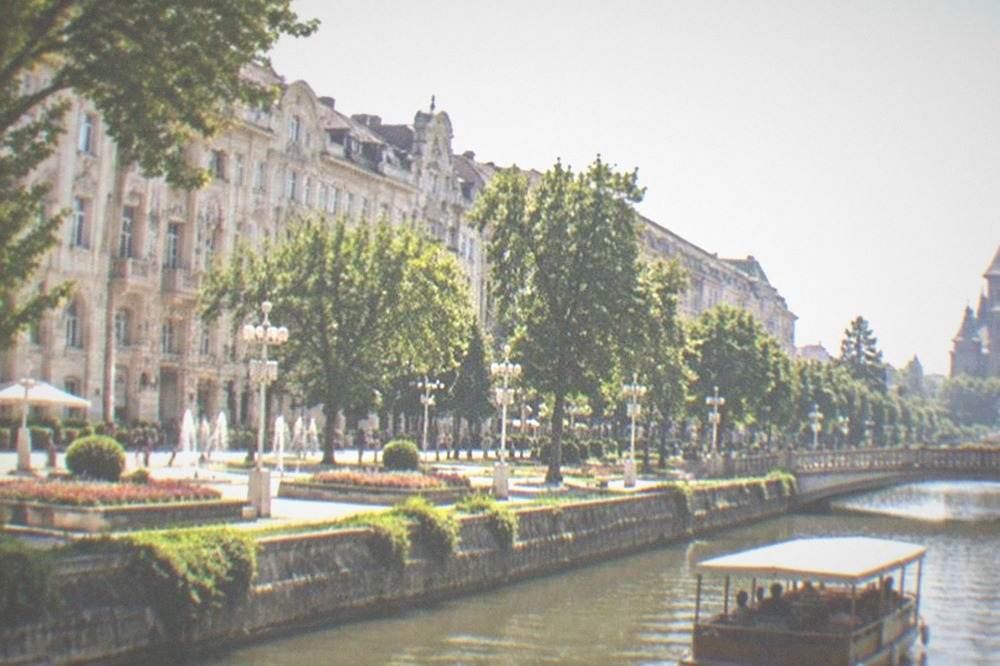 A canal boat passing tree-lined banks and a bridge in a European city