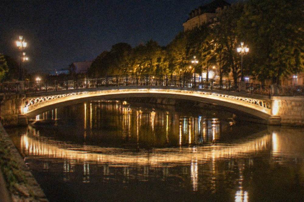 A night view of a lit bridge over a city canal with reflections on the water